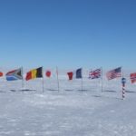 A propellor areoplane next to the flags of the Antarctic Treaty nations, behind the south pole marker